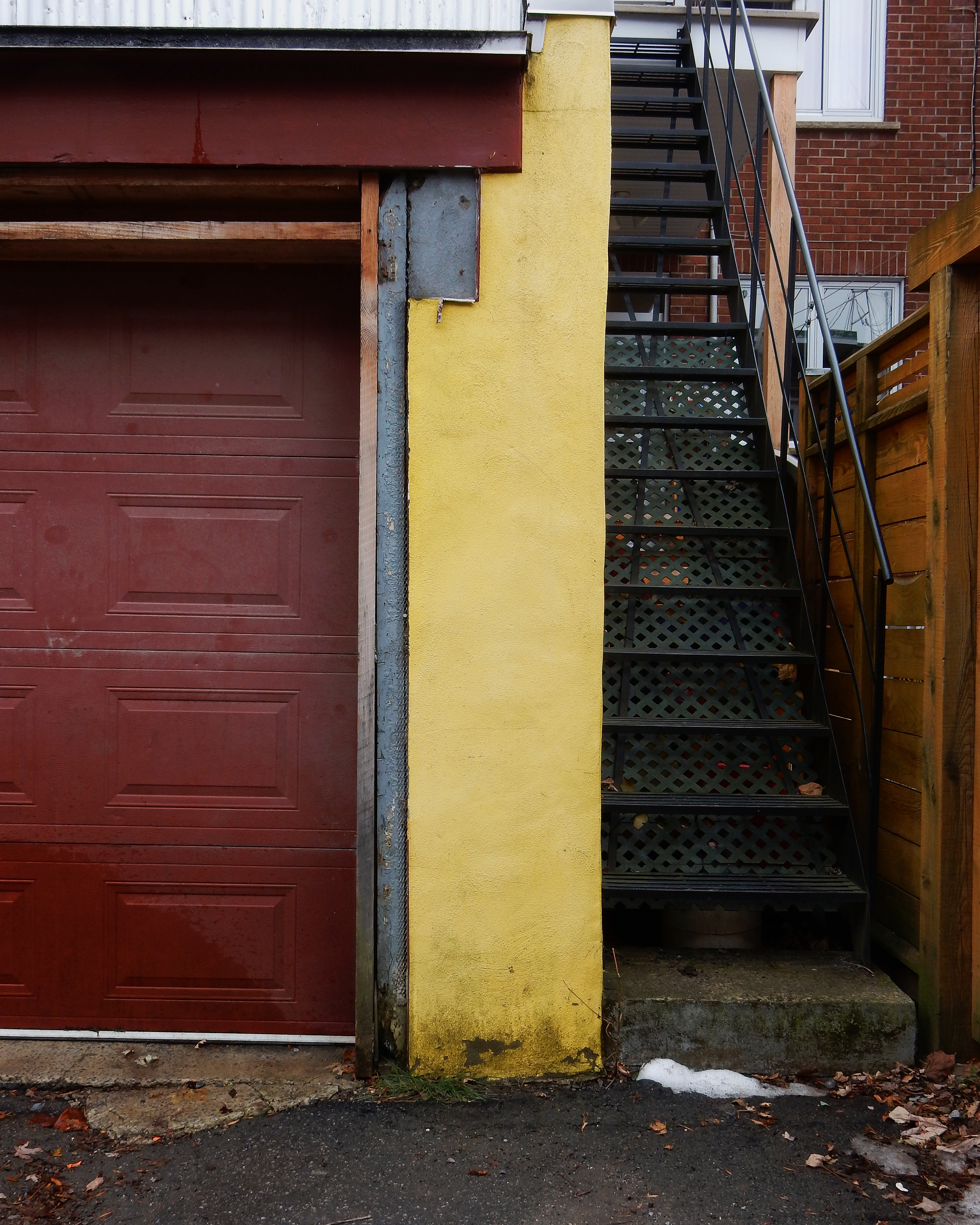Garage jaune moutarde avec une porte rouge foncé.